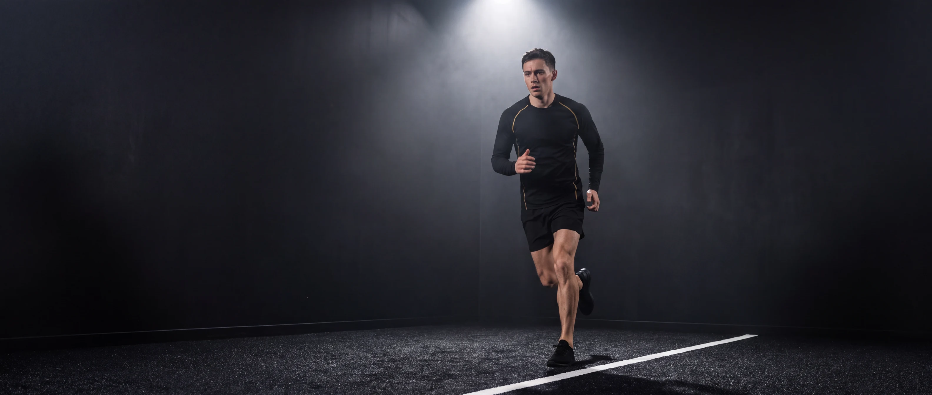 Lone athlete running on dark HYROX turf under a single spotlight, training alone